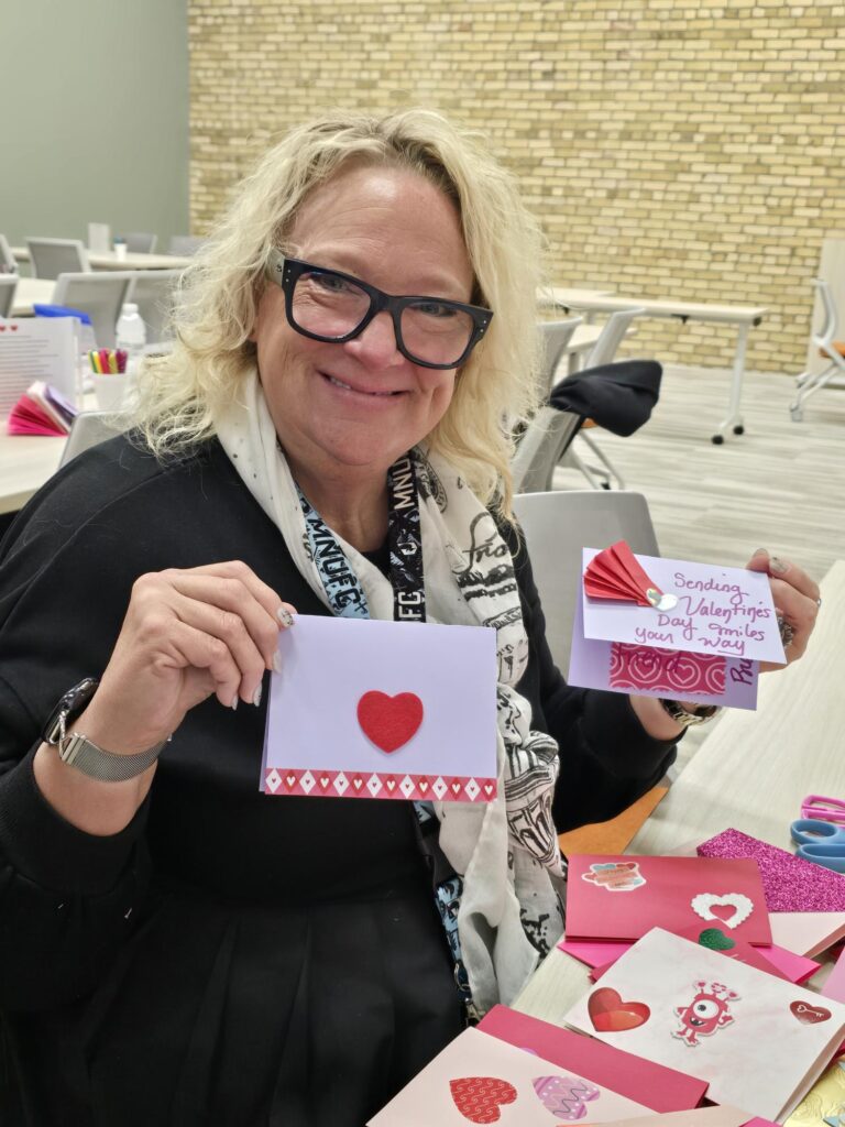Volunteer holding up two handmade valentines day cards at Friends & Co card making event