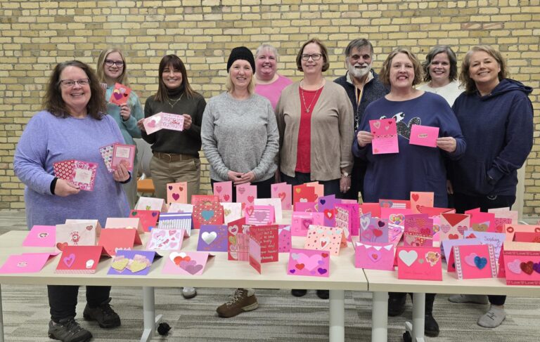Volunteers standing in a line in front of the 177 handmade valentines day cards they made for older adults with Friends & Co