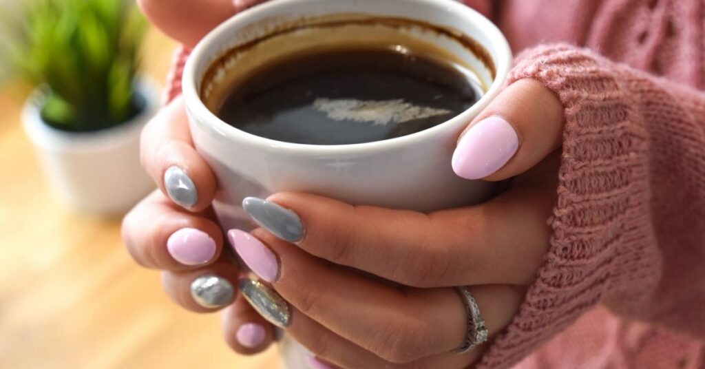 hands holding a cup of coffee with nails painted in pink and grey