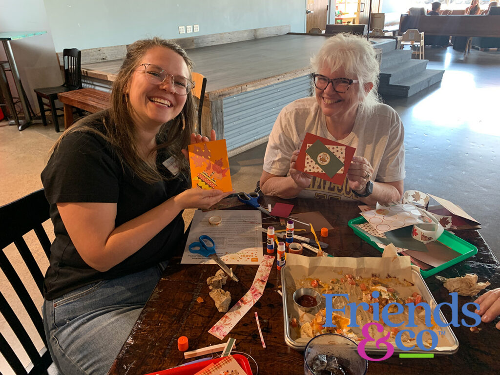 Volunteers smiling holding up some of their handmade cards for Friends & Co