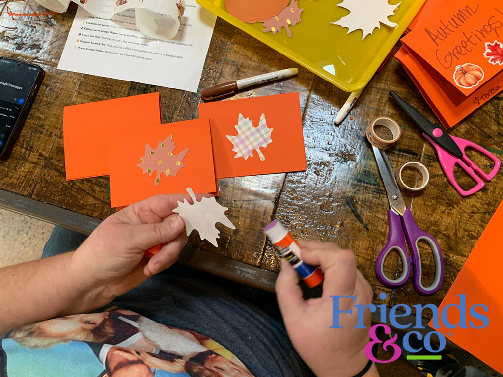 Volunteer applying a glue stick to some fall leaves for handmade cards